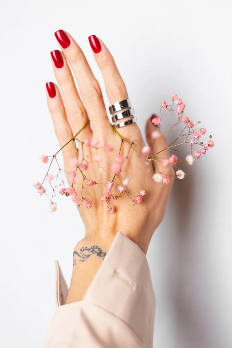Mano con manicure rojo sosteniendo pequeñas flores